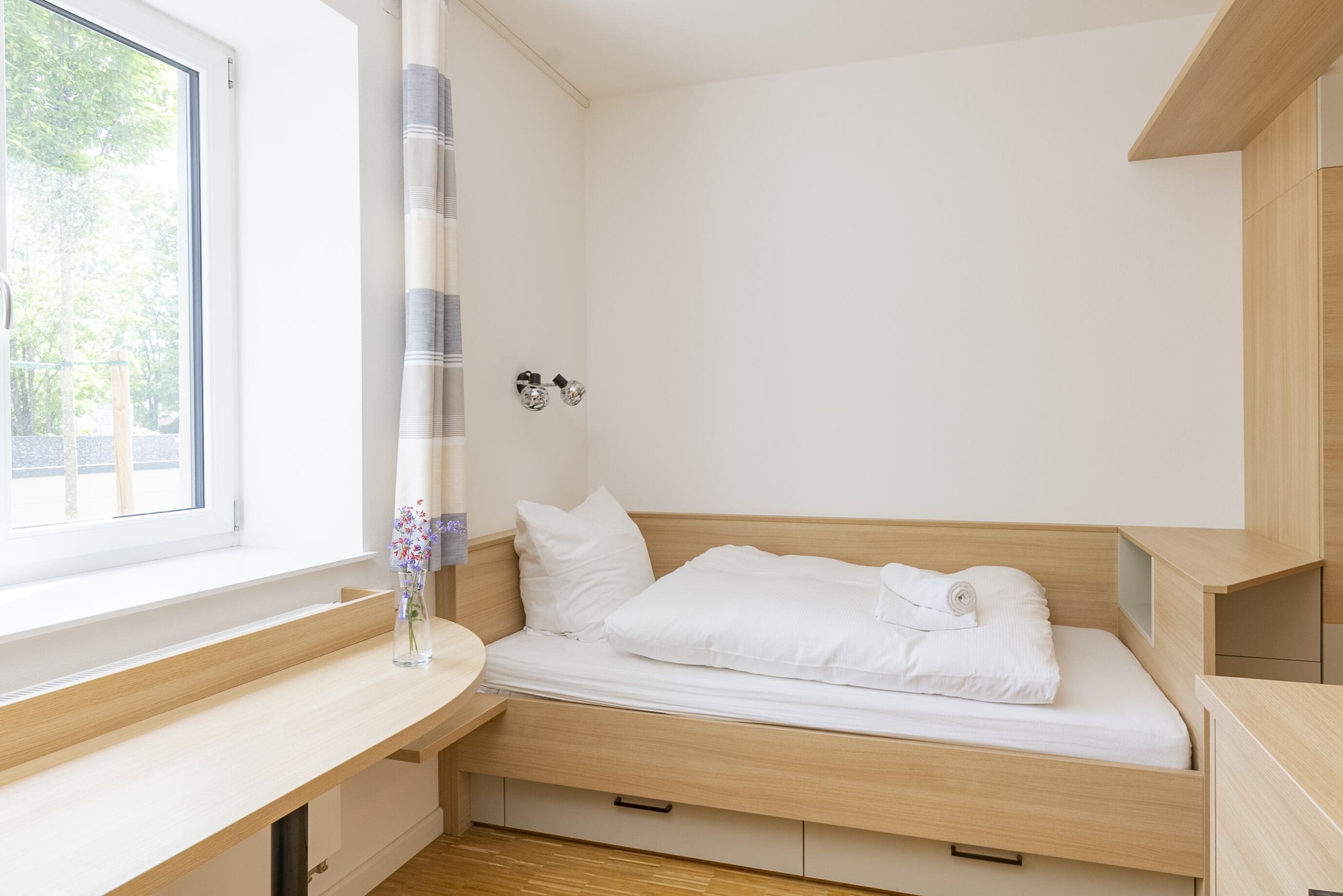 A bedroom with a bed, a window, a bedside table, and a small cabinet.