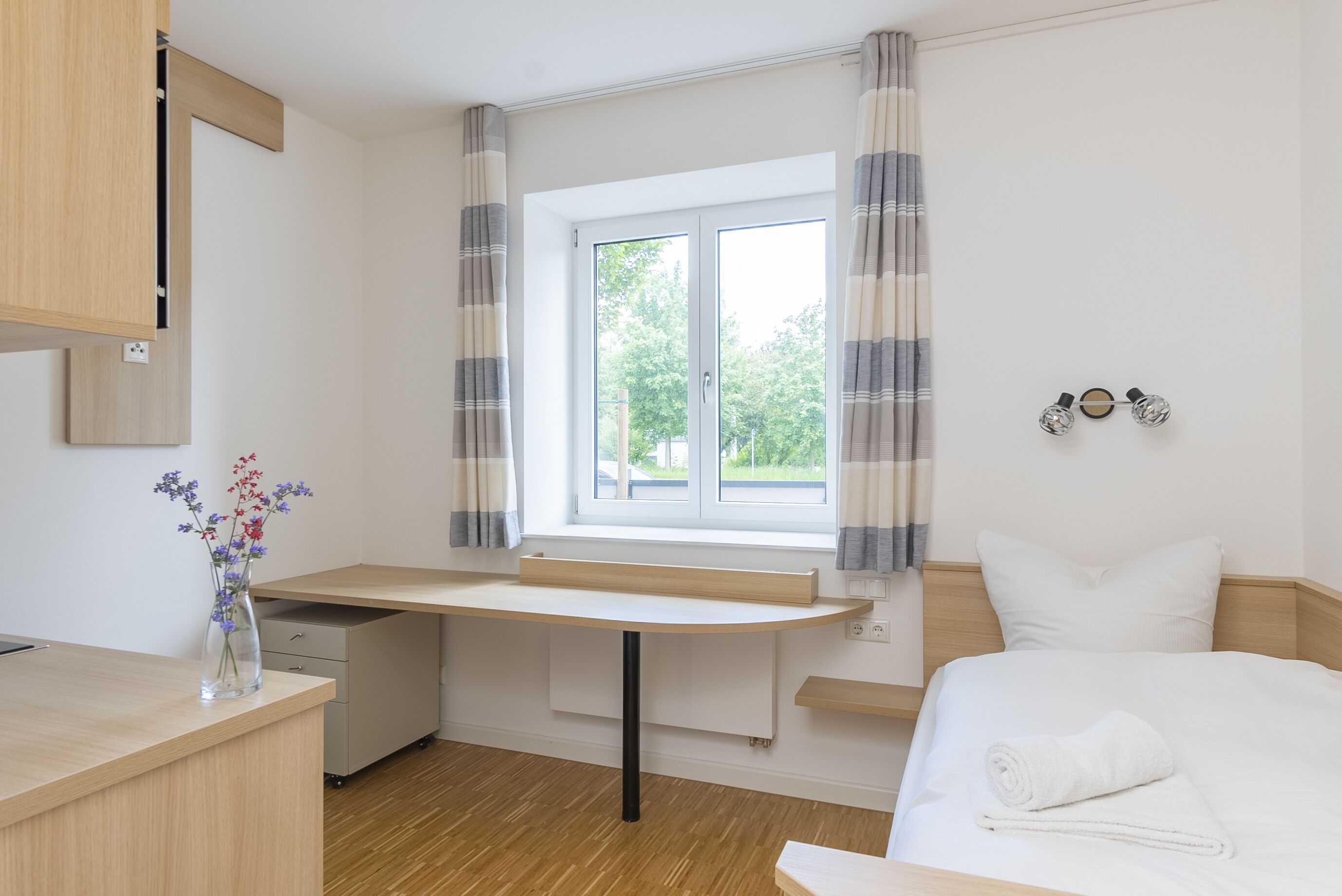 A bedroom with a bed, a desk, and a window with curtains.