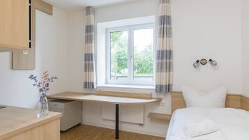 A bedroom with a bed, a desk, and a window with curtains.