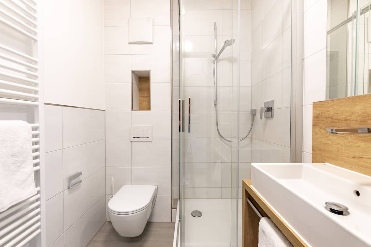 Un baño moderno con ducha de vidrio, inodoro blanco y tocador de madera con lavamanos.