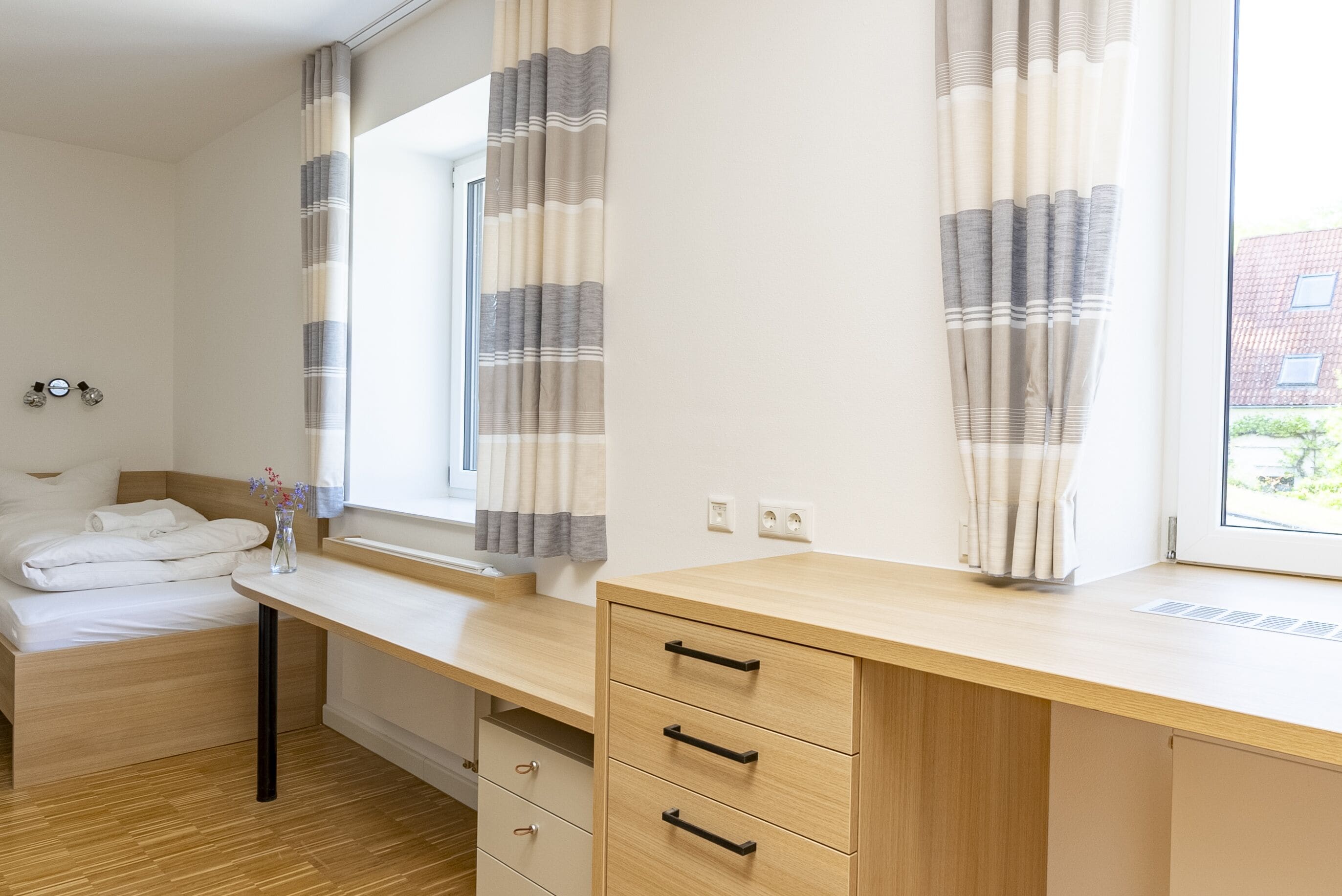 Ein Schlafzimmer mit einem Bett, einem Schreibtisch und einem Fenster mit Vorhängen.