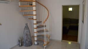 A spiral staircase with wooden steps and white railings, leading to a room with a sofa and a lamp.