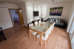 A modern living room with a glass dining table, a sofa, and a TV. - Apartments Ema - Superior Two-Bedroom Apartment with Balcony and Sea View (A3) (Zadar)