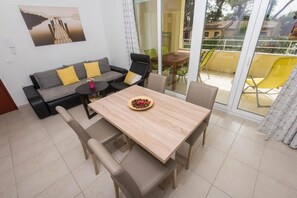 A modern living room with a sofa, a dining table, and chairs. There is a glass door leading to an outdoor area with yellow chairs. - Apartments Ema - One Bedroom Apartment with Balcony (A1) (Zadar)