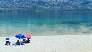 A beach with two umbrellas, a clear sky, and mountains in the background. - Apartments Branka - One Bedroom Apartment with Balcony (Razanac)
