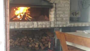 A stone fireplace with a fire burning inside, a stack of firewood, and a wooden bench in a room with tiled flooring. - Apartments Branka - One Bedroom Apartment with Balcony (Razanac)