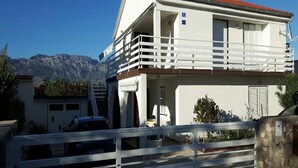 A two-story building with a balcony, a garage, and a mountain backdrop. - Apartments Branka - One Bedroom Apartment with Balcony (Razanac)