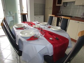 A dining table set with white plates, silverware, and wine glasses, covered with a white tablecloth and a red runner.