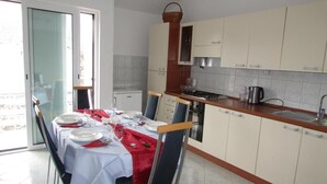 A dining area with a table set for four, a kitchen with white cabinets, and a sliding glass door leading to an outdoor area. - Apartments Branka - One Bedroom Apartment with Balcony (Razanac)