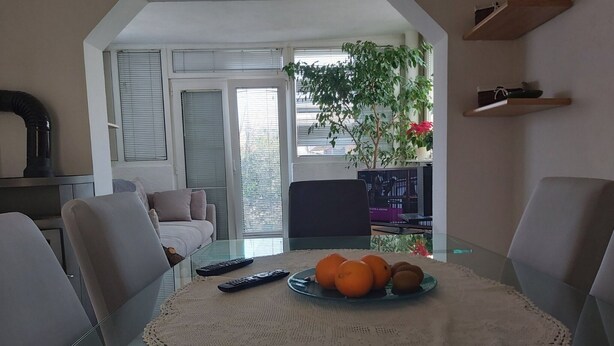 A dining area with a glass table, a white tablecloth, and a plate of oranges. There are chairs around the table, and a TV is visible in the background. - Apartments Branka - Two Bedroom Apartment with Terrace (Razanac)