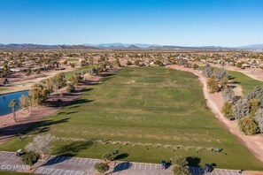 An aerial view of a golf course with a parking area, a lake, and a residential area in the background.