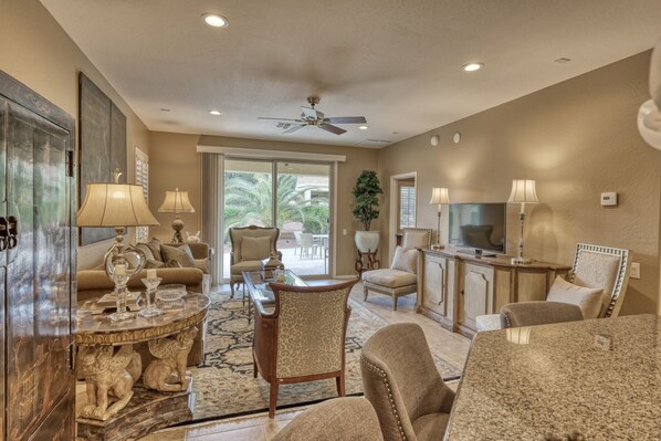 A spacious living room with a large TV, comfortable seating, and a ceiling fan.
