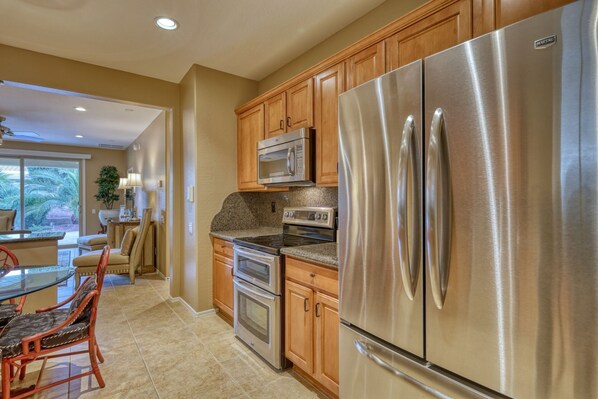 A modern kitchen with stainless steel appliances, wooden cabinets, and a dining area with a glass table and chairs. - Private Villa at Corte Bella Country Club (Sun City West)