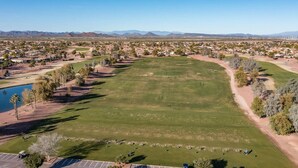 An aerial view of a golf course with a parking area, a lake, and a residential area in the background.