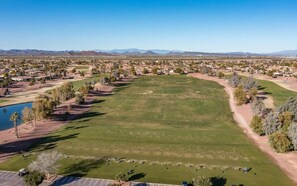 An aerial view of a golf course with a parking area, a lake, and a residential area in the background. - Private Villa at Corte Bella Country Club (Sun City West)