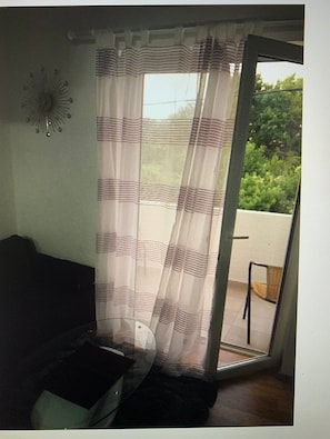 A room with a sofa, a chair, a curtain, and a view of greenery outside. - Apartments Vranela- One Bedroom Apartment With Balcony (Biograd na Moru)