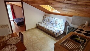 Eine kleine Küche mit Spüle und Herd, ein Holztisch mit Stühlen, ein Sofa mit gemustertem Bezug und ein Oberlicht.