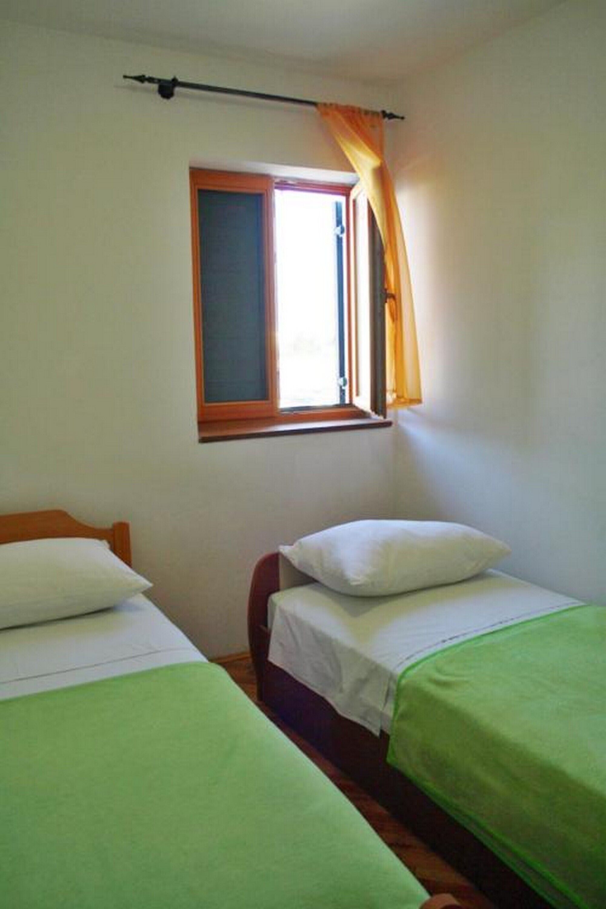 A room with two single beds, a window with curtains, and a wooden headboard.