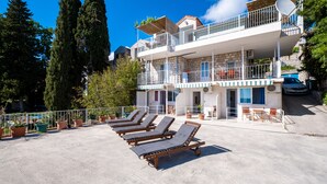Ein Hotel mit Dachterrasse, ausgestattet mit Liegestühlen, Blumentöpfen und Blick auf hohe Bäume und einen strahlend blauen Himmel.