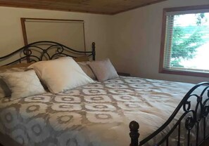 Een slaapkamer met een bed, een raam en een houten plafond.