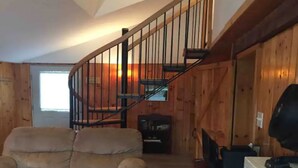 A wooden interior with a curved staircase, a sofa, and a television. - Belgrade Lakes McGrath Pond (Oakland)