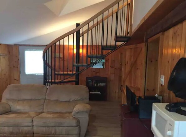 Un intérieur en bois avec un escalier en colimaçon, un canapé et un téléviseur.