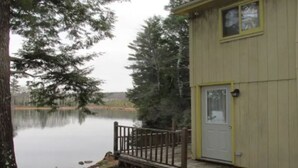 A wooden cabin by a calm lake, with a dock extending into the water. - Belgrade Lakes McGrath Pond (Oakland)