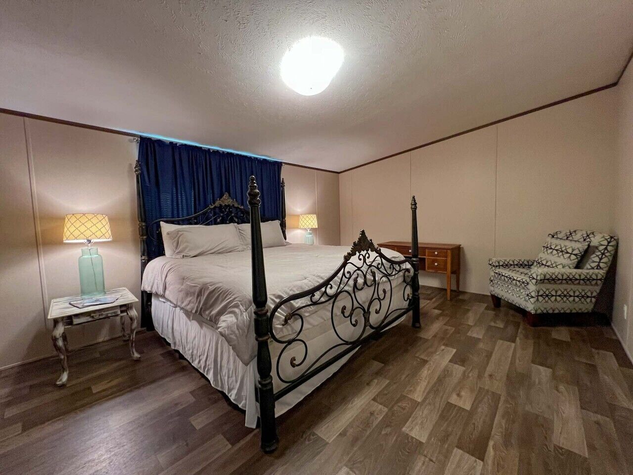 Une chambre à coucher avec un lit à baldaquin, une table de chevet avec une lampe, une chaise et un plancher en bois.