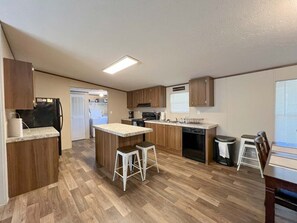 Una cocina compacta con armarios de madera, una isla central, taburetes de bar y lavavajillas.