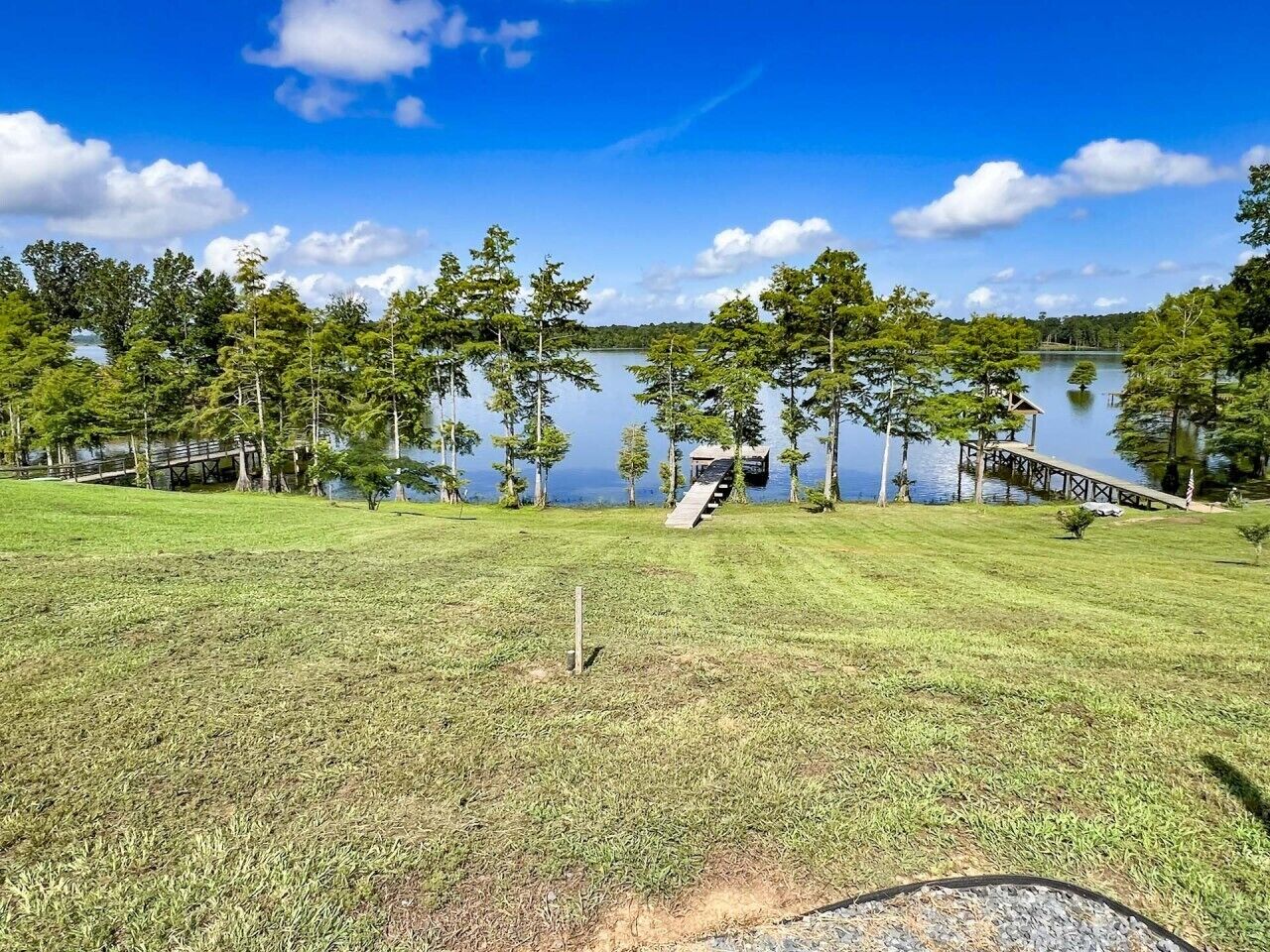 Zona verde con cubierta de madera y pequeño puente sobre un lago.