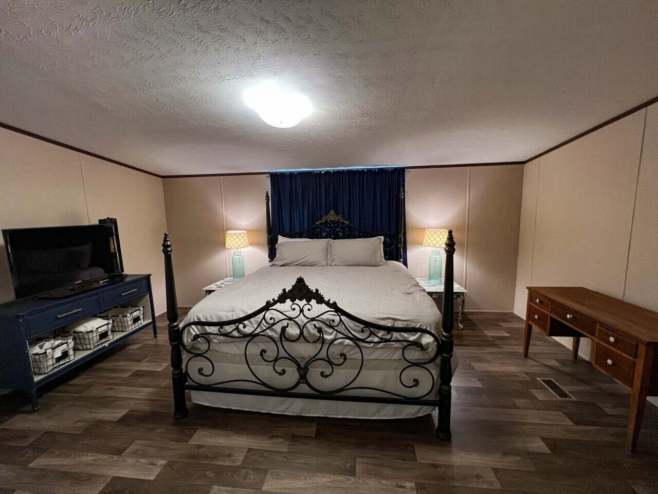 A bedroom with a four-poster bed, a television on a dresser, bedside lamps, and a wooden bench.