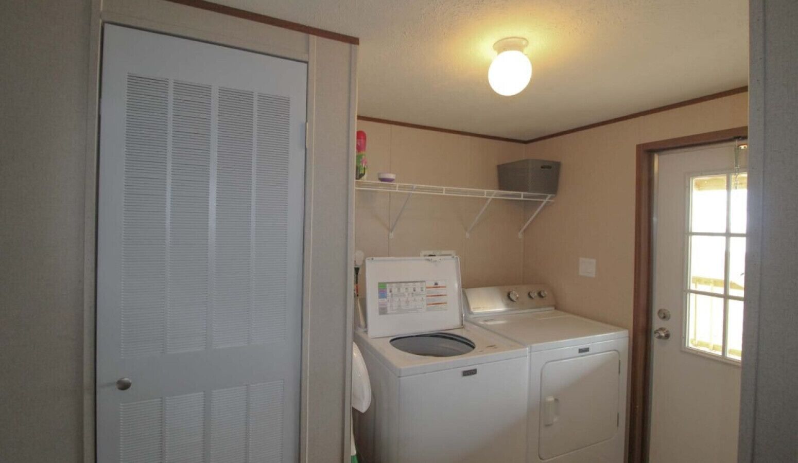 Un cuarto de lavado con lavadora y secadora, un estante sobre la secadora, y una puerta con ventana.