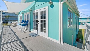 Een turquoise gebouw met een overdekt terras, witte relingen en blauwe stoelen.
