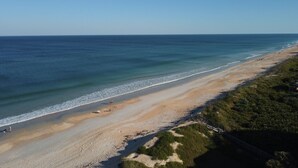 Een strand met een helder uitzicht op de oceaan, een zandstrand en wat begroeiing aan de rechterkant.