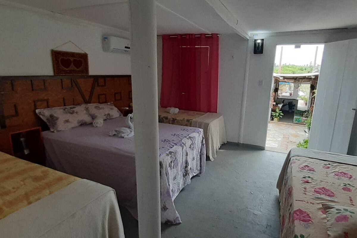 Une chambre avec deux lits, une tête de lit en bois, un rideau rouge et une vue sur l’extérieur.