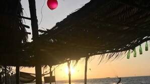 A beachside hut with a table and chairs under a thatched roof, overlooking the sea with a sunset in the background. - Pousada Estresse Zero (Barreirinhas)