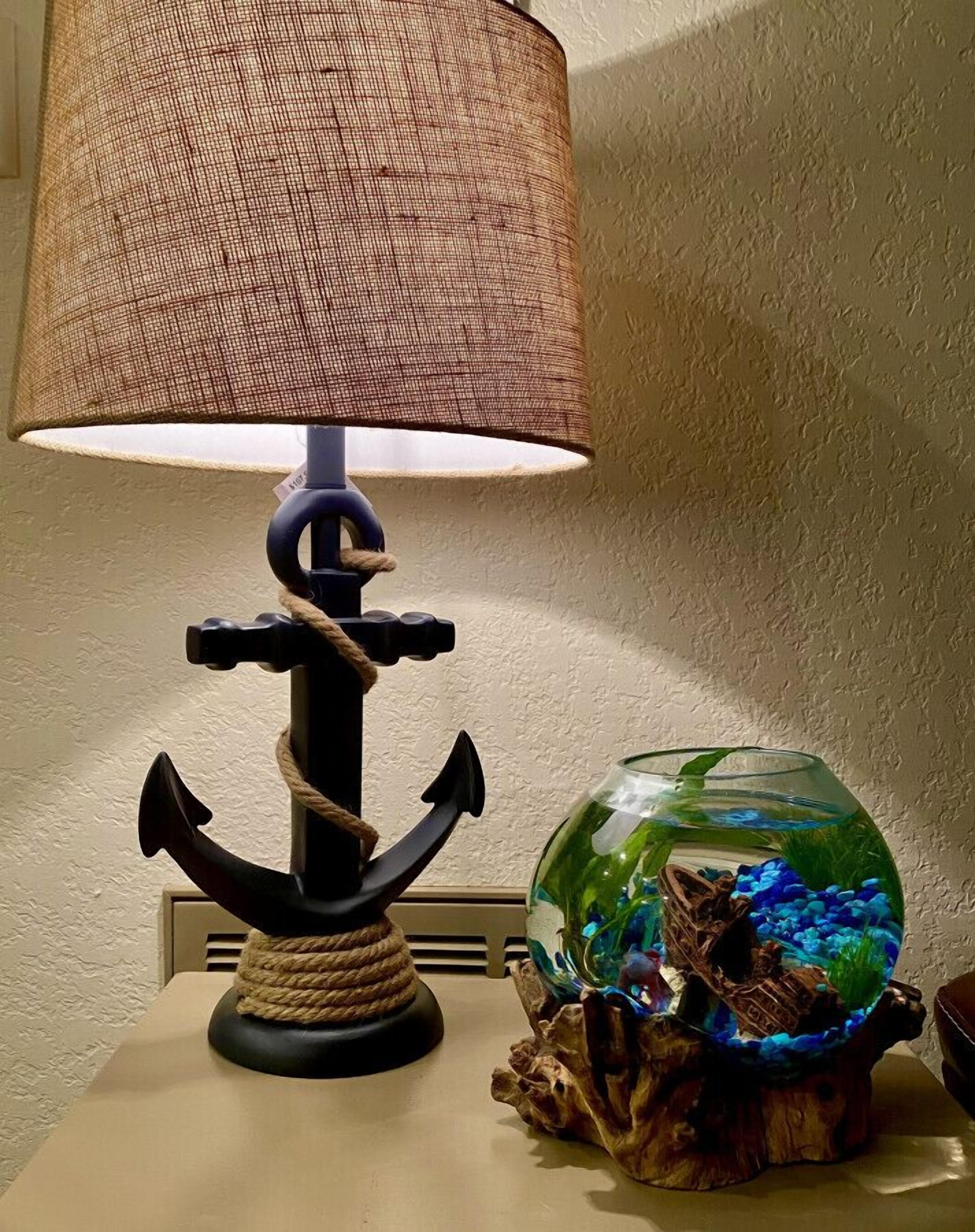 A table with a lamp featuring an anchor design and a fishbowl with aquatic plants.