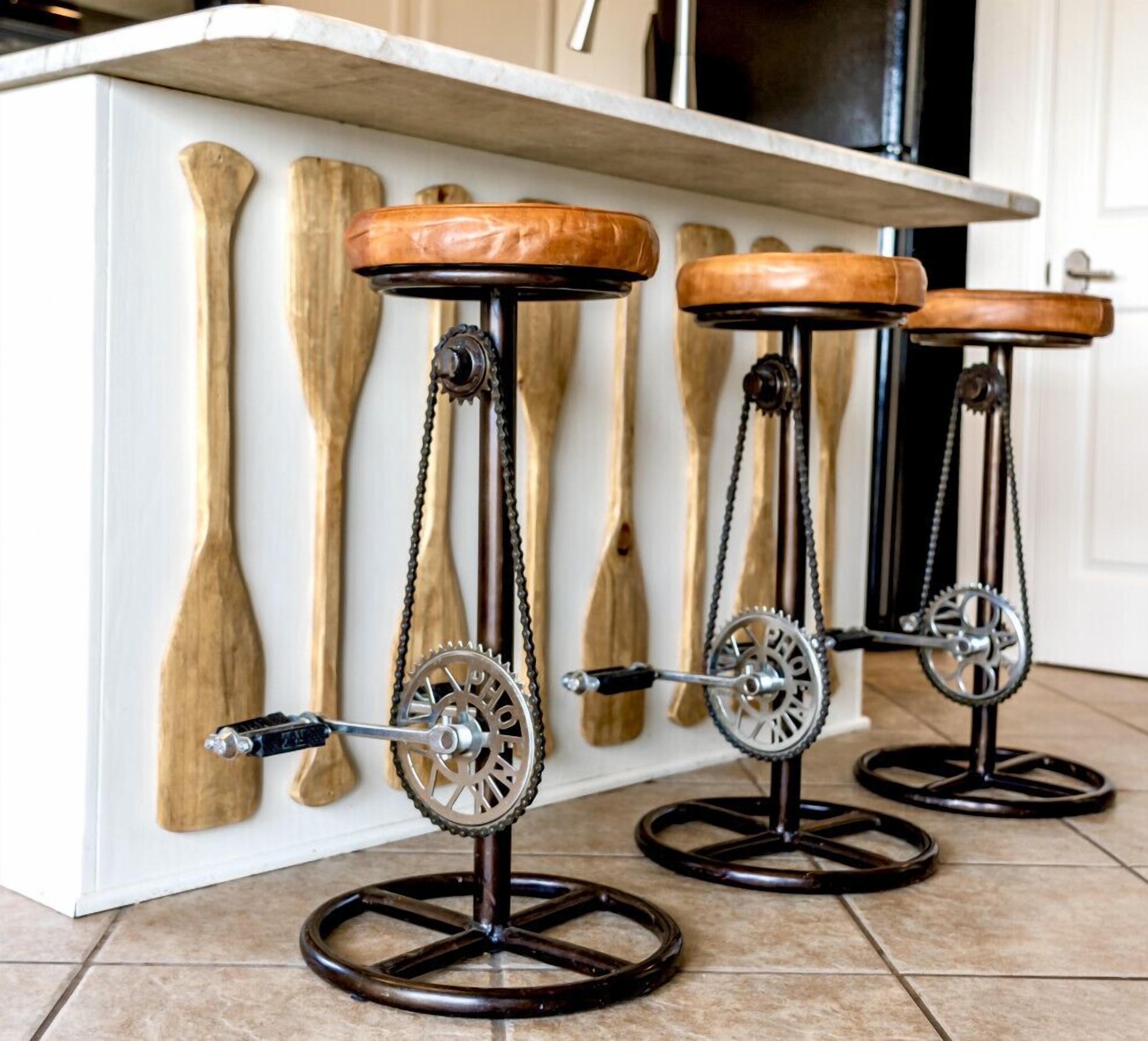 Three bar stools with wooden seats and metal bases, positioned against a kitchen island with wooden utensils hanging on the wall.