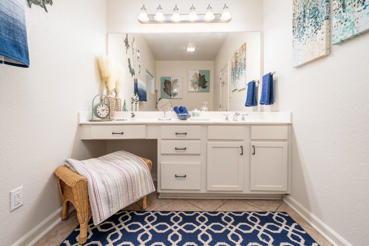 A bathroom with a white vanity, a mirror, a sink, and a bench.