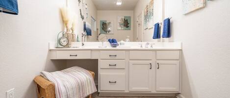 A bathroom with a white vanity, a mirror, a sink, and a bench.