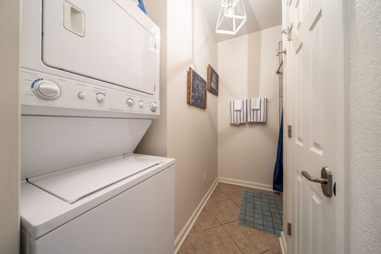 A laundry room with a front-loading washer and dryer, a towel rack, and a door leading to another room.