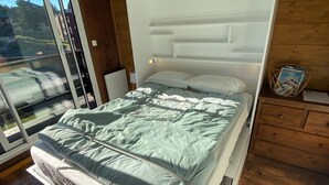 Un dormitorio moderno con una cama, suelo de madera y vistas a través de un ventanal corredero.