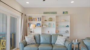 Een woonkamer met een lichtblauwe leren bank, een houten salontafel en een witte boekenkast vol boeken en decoratieve objecten.