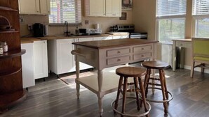Une cuisine avec des meubles blancs, un îlot central en bois et deux tabourets.