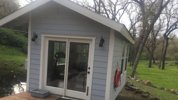 Une petite cabane dotée d’une terrasse en bois, d’une porte-fenêtre coulissante et d’un extincteur fixé au mur extérieur.