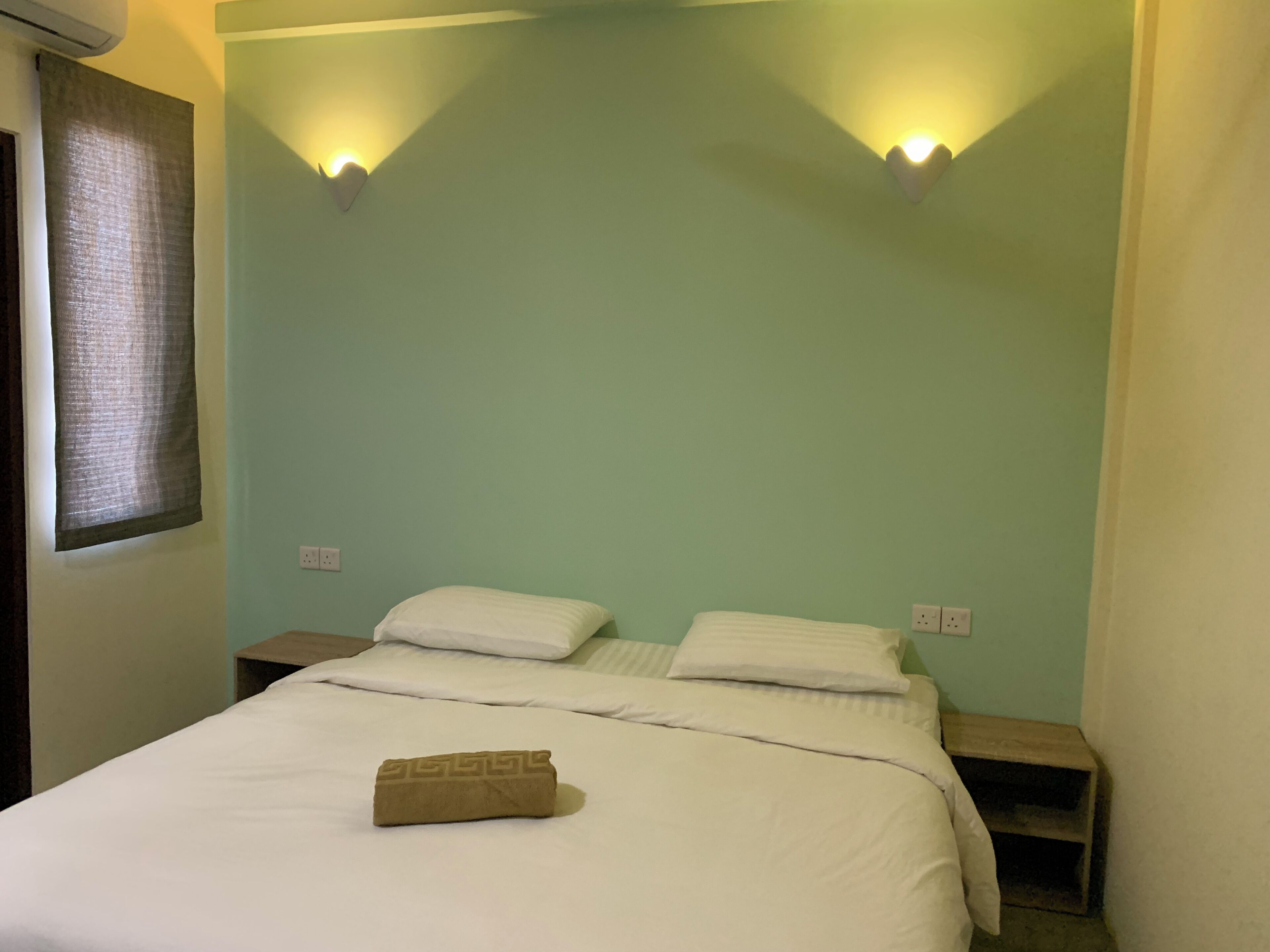 A single bed with white bedding, two bedside tables, and two wall-mounted light fixtures.