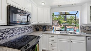 Una cucina moderna con mobili bianchi, un piano cottura nero e un'ampia finestra che si affaccia su un giardino.