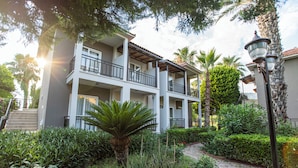 A multi-story building with balconies, surrounded by lush greenery and a paved pathway.