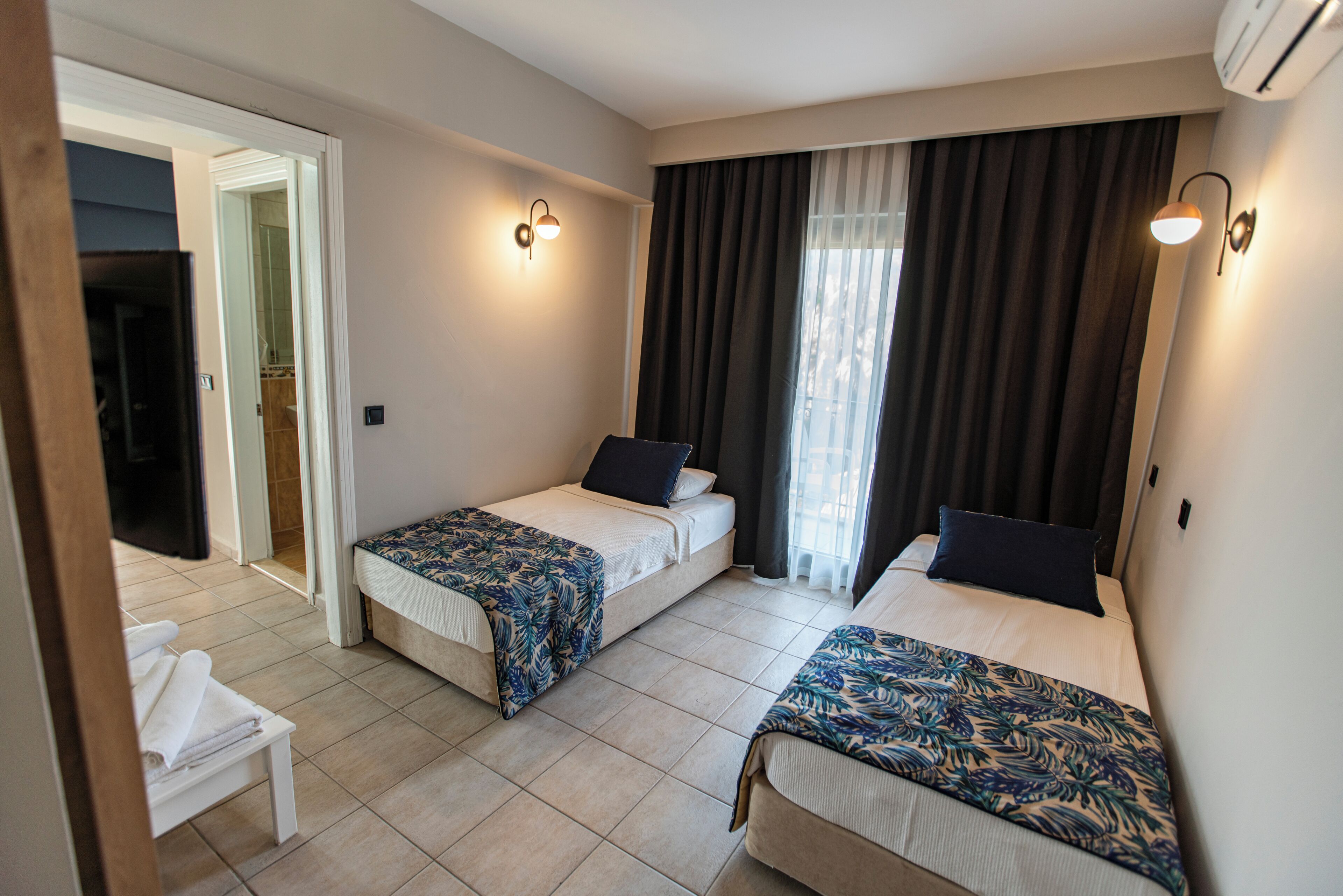A hotel room with two beds, a small seating area, and a bathroom visible through an open door.