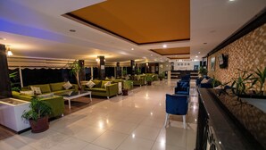 A hotel lobby with green sofas, a reception desk, and potted plants.